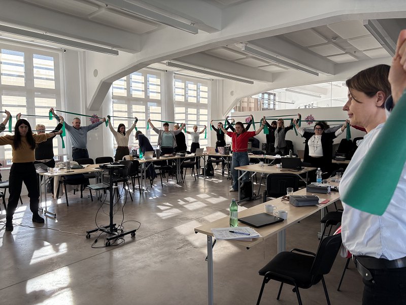 Udeleženci projektnega sestanka SUPPORTER med aktivnim odmorom vadijo z elastiko